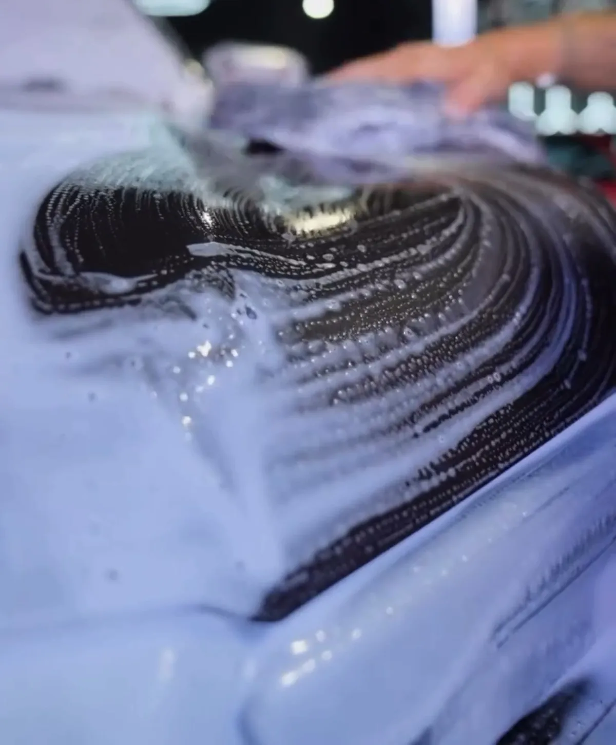 Wash mitt pushing thick foam across dark paint